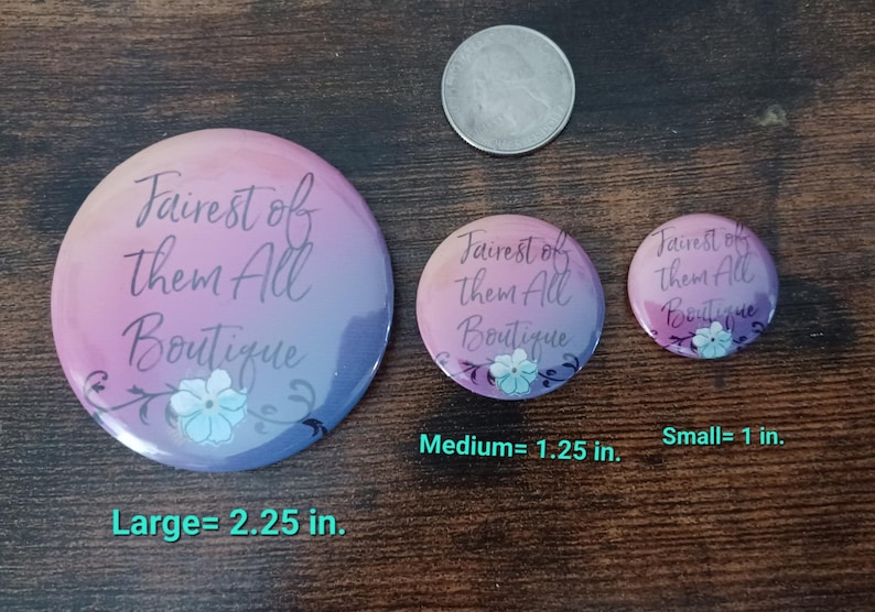 May include: Three round buttons with the text "Fairest of Them All Boutique" in a gradient of pink and purple. The largest button is 2.25 inches, the medium is 1.25 inches, and the smallest is 1 inch. Each button has a floral design.