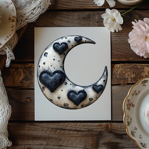 May include: A silver crescent moon with black hearts on a white background. The moon is decorated with a black and white speckled pattern.