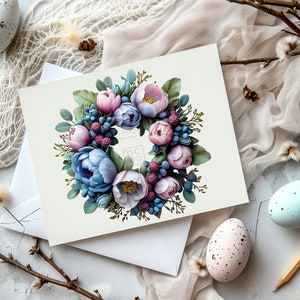K&ouml;nnte beinhalten: Eine wei&szlig;e Karte mit einer Illustration eines Blumenkranzes. Der Kranz besteht aus rosa und blauen Blumen mit gr&uuml;nen Bl&auml;ttern und Beeren. Die Karte liegt auf einem wei&szlig;en Umschlag.