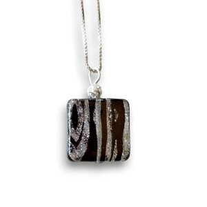May include: A silver chain necklace with a square pendant made of black glass with silver glitter accents.