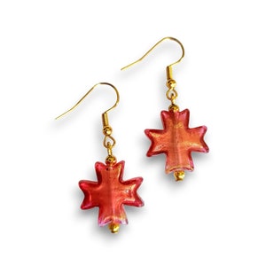 May include: A pair of gold earrings with red glass star-shaped charms. The charms have a metallic gold finish.