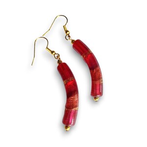 May include: A pair of red and gold earrings with a curved shape. The earrings are made of glass and have a gold leaf design.