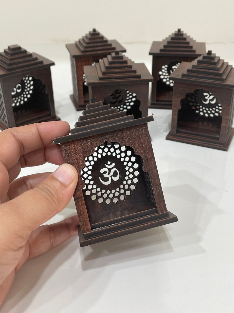 May include: Set of six small wooden temple-shaped boxes with intricate carvings and an "Om" symbol on the front. The boxes are dark brown and have a tiered roof.