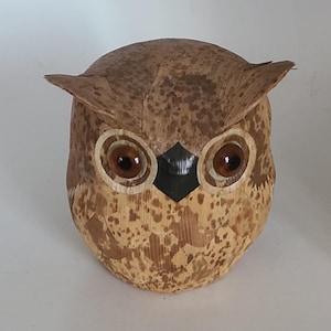 May include: A brown owl figurine made of woven palm leaves with large brown eyes. The owl has a black beak and is a decorative object.