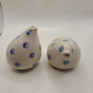 May include: Two ceramic cream-colored decorative pieces. One is pear-shaped, the other is round. Both are adorned with small blue floral patterns. Each piece has a small spout.