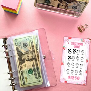 May include: A pink and white plastic card with a strawberry design and the text "SECTION one" and "$1250". The card has a grid of strawberries with numbers written on them. Some of the strawberries have an "X" over them.