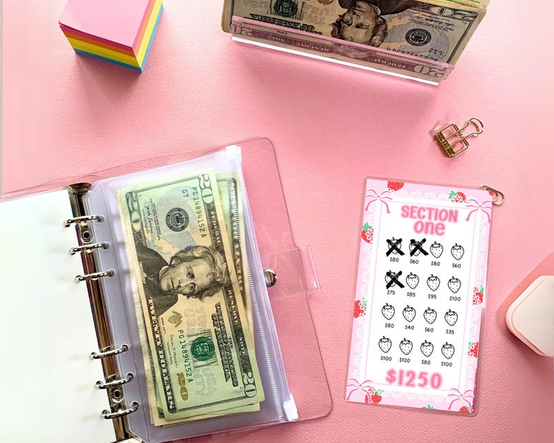 May include: A pink and white plastic card with a strawberry design and the text "SECTION one" and "$1250". The card has a grid of strawberries with numbers written on them. Some of the strawberries have an "X" over them.