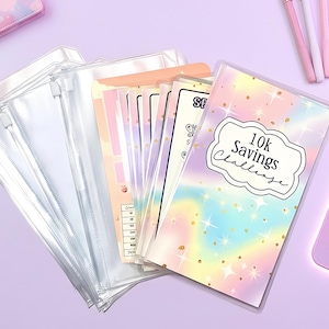 May include: A collection of clear zippered pouches and colorful inserts, including a notebook with a pastel rainbow design and the text "10K Savings Challenge." The items are arranged on a light purple surface, with pens and a mouse visible.