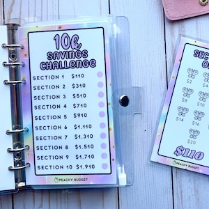 May include: A clear binder with a savings challenge insert. The insert reads "10k Savings Challenge" with sections and amounts. A separate card shows a "Section One" scratch-off style savings game with butterfly graphics.