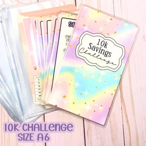May include: A set of A6 size savings challenge envelopes. The front envelope has a pastel rainbow design with gold glitter and the text "10K Savings Challenge". Additional envelopes are visible, along with the text "10K Challenge SIZE A6".