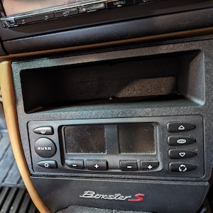 Puede incluir: Primer plano de un salpicadero de coche negro con un compartimento de almacenamiento, una pantalla digital con botones y el texto "Boxster S".