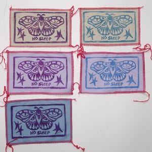 Op de afbeelding: Vijf stoffen patches met een paars en blauw vlinderontwerp en de tekst "NO SLEEP" erop gedrukt. De patches zijn op een witte achtergrond.