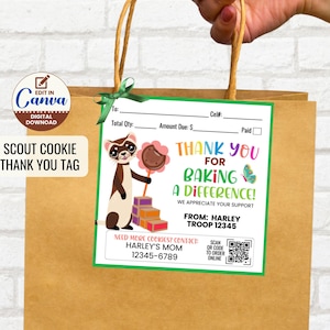 以下が含まれることがあります： 「ありがとう、違いを生み出すために！」と書かれた緑と白のタグが付いた茶色の紙袋。漫画のフェレットがクッキーを持っています。バッグには「Scout Cookie Thank You Tag」というテキストも表示されています。
