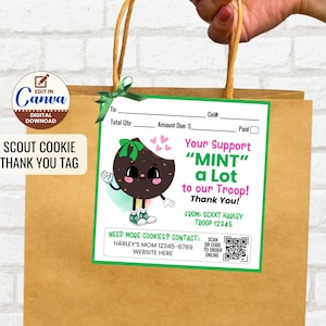 Peut inclure: Un sac cadeau en papier brun avec une étiquette verte et blanche. L'étiquette présente un personnage de biscuit de dessin animé et le texte "Your Support 'MINT' a Lot to our Troop! Thank You!" et "Scout Cookie Thank You Tag."