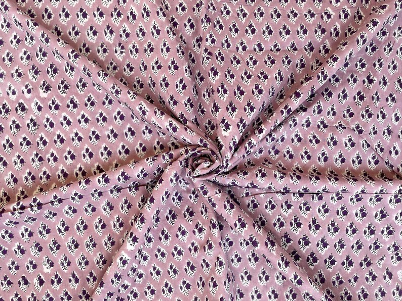 Puede incluir: Primer plano de una tela con un patr&oacute;n repetido de peque&ntilde;as formas florales de color p&uacute;rpura oscuro sobre un fondo malva claro. La tela est&aacute; reunida y doblada, mostrando la textura y la ca&iacute;da del material.
