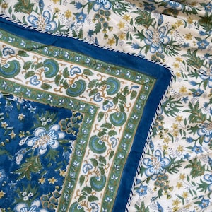 May include: A floral patterned textile featuring a blue border and a white background. The design includes blue, green, and yellow flowers and foliage. The border is a solid blue with a white trim.