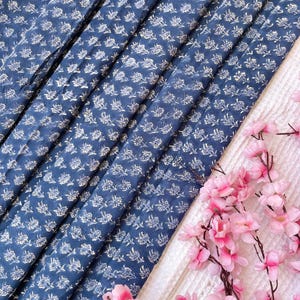 May include: Blue fabric with a white floral pattern. The fabric is folded in several layers and has a soft, textured feel.