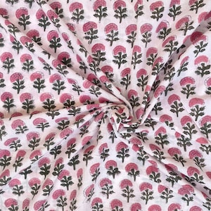 May include: White fabric with a repeating pattern of pink floral blooms and dark green stems. The fabric is arranged in soft folds, showcasing the all-over floral design. The pattern is a block print style.