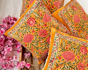 Puede incluir: Cuatro almohadas cuadradas con un patrón floral en tonos amarillos, naranjas, rosas y verdes. Las almohadas tienen un borde blanco.