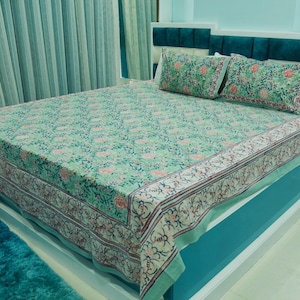 May include: A bed dressed with a light green floral patterned bedspread and two matching pillowcases. The bedspread and pillowcases feature a repeating pattern of pink flowers and green leaves. The bed is set against a teal headboard.