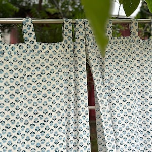 Peut inclure: Rideaux à motifs floraux blancs et bleus suspendus à une tringle en métal. Les rideaux présentent un motif répétitif de petites fleurs bleues sur fond blanc. Les rideaux sont suspendus devant un fond vert.