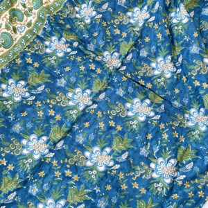 May include: A blue fabric with a floral pattern. The design features large white and light blue flowers, green leaves, and small yellow star-shaped accents. A border with a green and white floral pattern is visible.