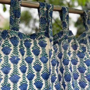 Puede incluir: Primer plano de cortinas con estampado floral azul y blanco. Las cortinas cuelgan de una barra de metal. El estampado floral presenta flores azules y hojas verdes sobre un fondo blanco. Las cortinas son de tela ligera.