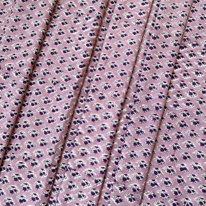 Puede incluir: Primer plano de una tela con un patr&oacute;n floral repetido. La tela es de color rosa polvoriento con un patr&oacute;n de peque&ntilde;as flores moradas oscuras y acentos blancos. La tela est&aacute; doblada en pliegues verticales.