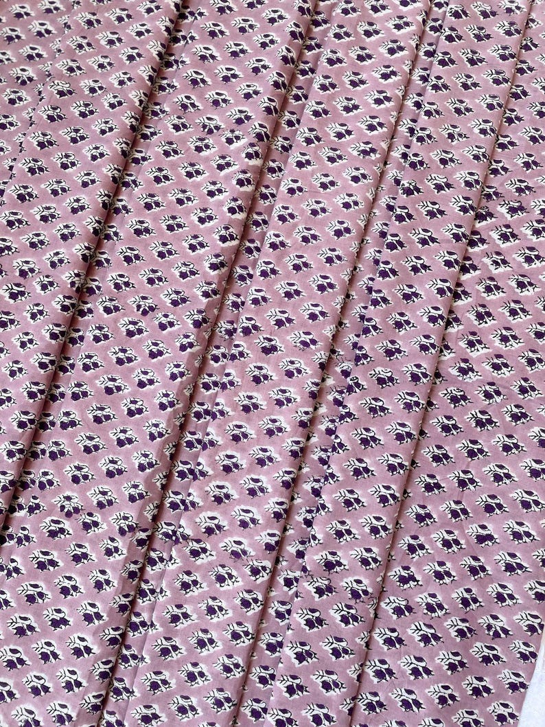 Puede incluir: Primer plano de una tela con un patr&oacute;n floral repetido. La tela es de color rosa polvoriento con un patr&oacute;n de peque&ntilde;as flores moradas oscuras y acentos blancos. La tela est&aacute; doblada en pliegues verticales.
