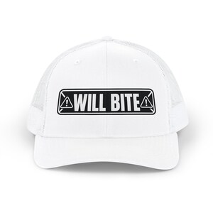 May include: A white trucker hat featuring a black rectangular patch on the front panel. The patch displays the text WILL BITE in bold capital letters, flanked by two small triangular warning icons containing exclamation marks on each side.