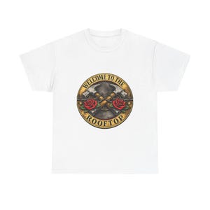 Peut inclure: Un t-shirt blanc à manches courtes avec un motif circulaire sur la poitrine. Le design présente deux marteaux croisés, deux roses rouges et du fil barbelé, entourés par le texte "WELCOME TO THE ROOFTOP" dans une bordure circulaire dorée.