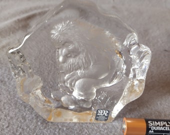 May include: A clear glass sculpture of a gnome sitting with a beard and a hat. The sculpture is made by the artist Mats Jonasson and is signed on the bottom.