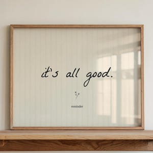 Könnte beinhalten: Ein gerahmter Druck mit den Worten "it's all good" in schwarzer Schrift. Der Druck befindet sich in einem hellen Holzrahmen und ruht auf einem passenden Holzregal. Eine kleine Blumenillustration und das Wort "reminder" stehen darunter.
