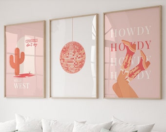 Op de afbeelding: Drie ingelijste prints met een roze achtergrond. De linker print toont een rode cactus met de tekst "Cowgirls don't cry" en "Wild West". De middelste print toont een zilveren discobal die aan een touwtje hangt. De rechter print toont een paar rode cowboylaarzen met de tekst "Howdy" die vier keer wordt herhaald.