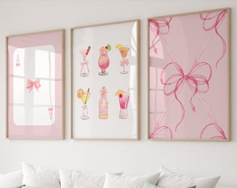 May include: Three framed prints with pink backgrounds. The left print features a pink bow and the letter A. The center print features a watercolor illustration of pink cocktails. The right print features a pink bow with pink ribbons.
