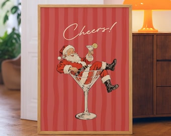 May include: A framed print featuring Santa Claus relaxing in a martini glass, holding a cocktail with a lemon slice. The background is red with vertical stripes, and the word "Cheers!" is written in cursive.