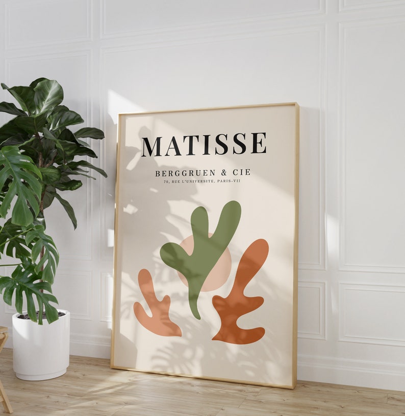 May include: A beige poster with a gold frame featuring a Matisse art print. The poster has a green, orange, and pink abstract design with the text "MATISSE" and "BERGGRUEN & CIE 70, RUE DE L'UNIVERSITE, PARIS-VII" in black.