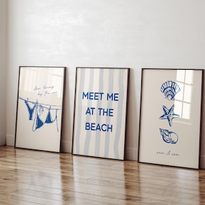 May include: Three framed art prints with a beach theme. One print shows a blue bikini hanging on a clothesline with the text "slow living by the sea." Another says "MEET ME AT THE BEACH." The third features seashells and the words "sun & sea."