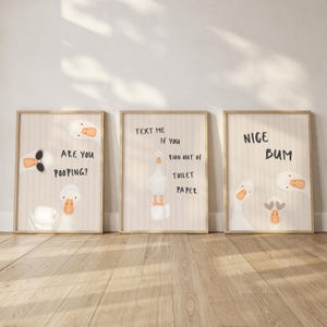 May include: Three framed wall art prints featuring cartoon geese on a light beige striped background. The first print says ARE YOU POOPING? The second says TEXT ME IF YOU RUN OUT OF TOILET PAPER. The third print features the text NICE BUM.