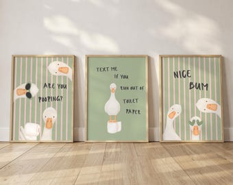 May include: Three framed wall art prints featuring white geese on sage green backgrounds. The first print has pink stripes and text reading ARE YOU POOPING?. The second print shows a goose on toilet paper with text reading TEXT ME IF YOU RUN OUT OF TOILET PAPER. The third print has pink stripes and text reading NICE BUM.