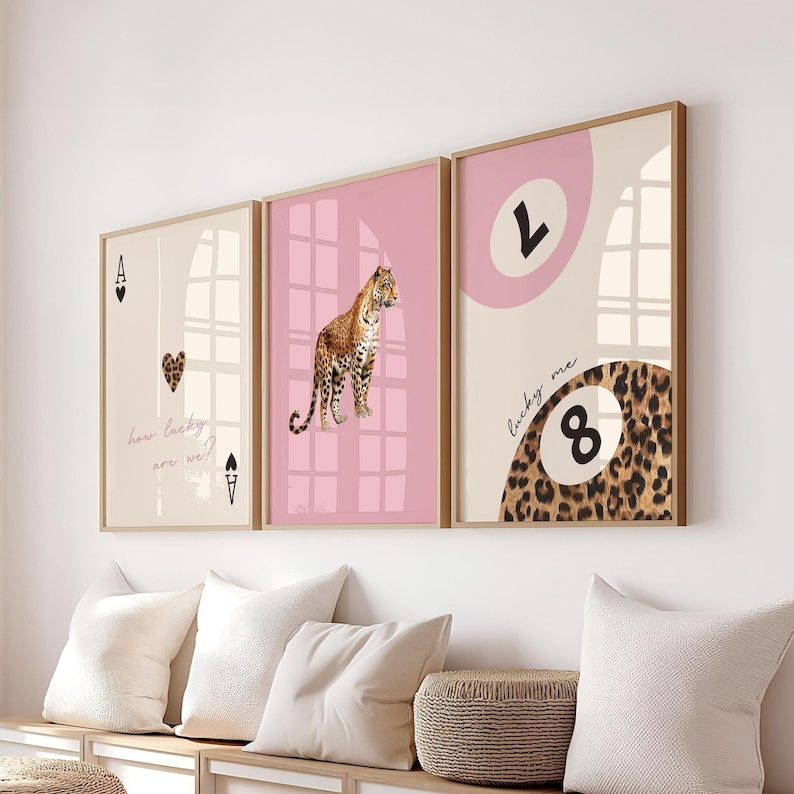 May include: Three framed prints in a pink and beige colour scheme. The left print features a playing card with an ace of spades and the text "how lucky are we?" The middle print features a leopard print and the text "lucky me". The right print features a leopard print with a pink circle and the number "8" inside.