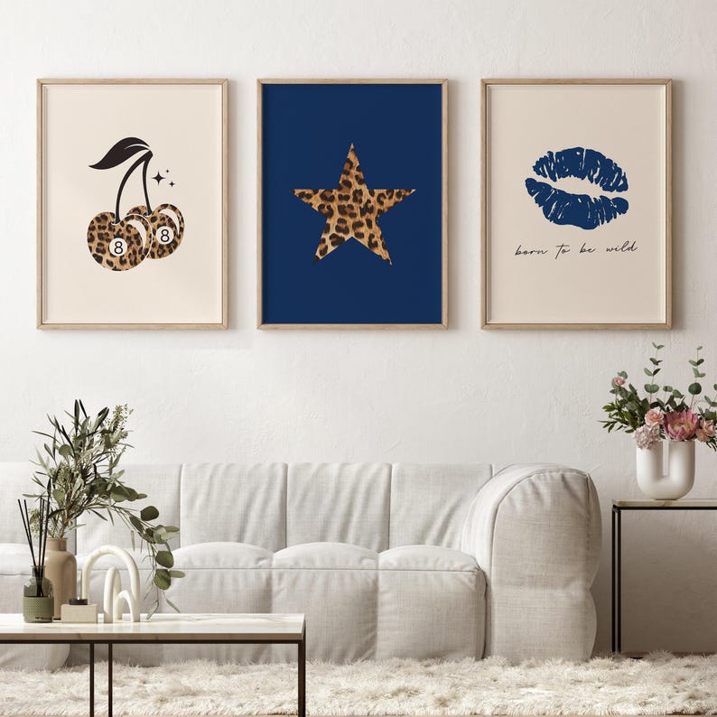 Op de afbeelding: Drie ingelijste prints met een witte achtergrond. De linker print toont een zwarte kers met een luipaardprint en het nummer 8 op elke kers. De middelste print toont een blauwe achtergrond met een luipaardster. De rechter print toont een witte achtergrond met een blauwe lipafdruk en de tekst "born to be wild".