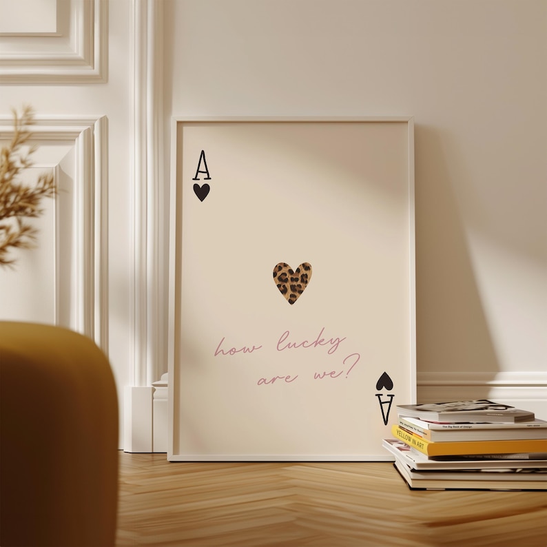 May include: A beige poster featuring a black ace of spades playing card with a leopard print heart in the centre. The text "how lucky are we?" is written in pink below the heart.
