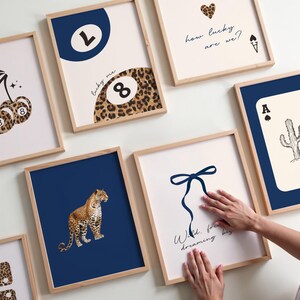 Op de afbeelding: Een set van negen ingelijste prints met verschillende ontwerpen. De prints bevatten een luipaardprint, een blauwe achtbal, een blauwe strik, een speelkaart, een kers en een hart. De prints zijn allemaal in houten lijsten.