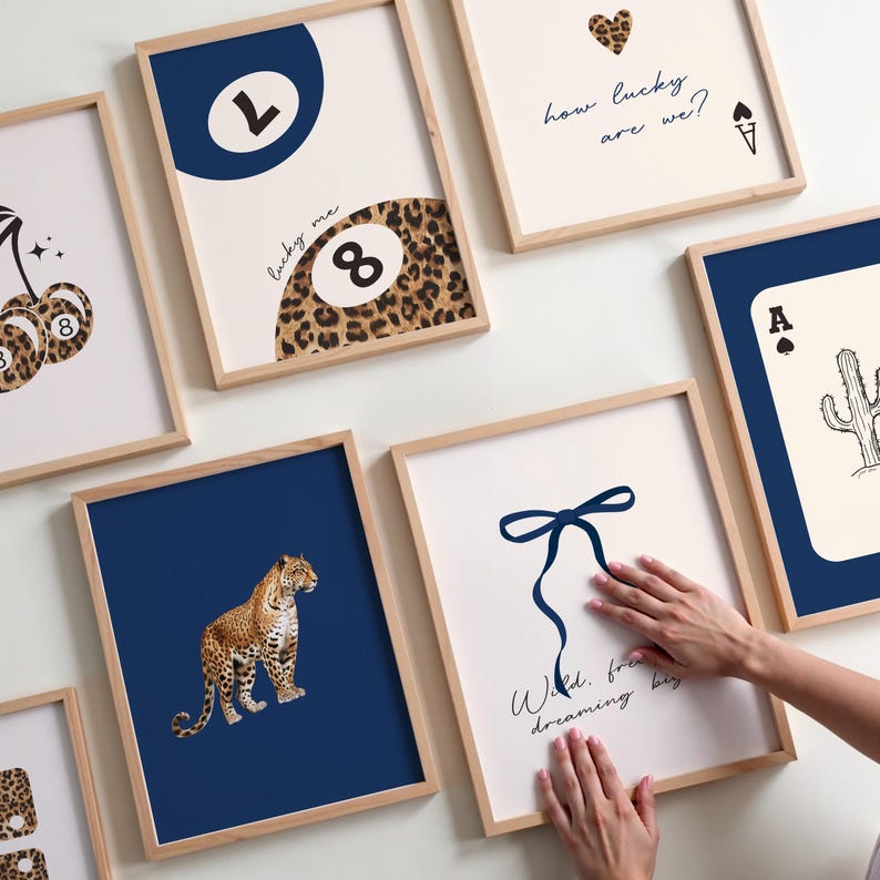 Op de afbeelding: Een set van negen ingelijste prints met verschillende ontwerpen. De prints bevatten een luipaardprint, een blauwe achtbal, een blauwe strik, een speelkaart, een kers en een hart. De prints zijn allemaal in houten lijsten.
