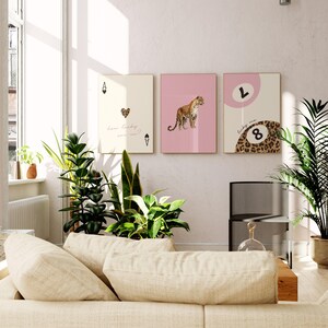 May include: Three pink and cream framed prints with a leopard print design. The left print features a playing card with a heart and the text "how lucky are we?" The middle print features a leopard. The right print features a leopard print with a large number 8 and the text "lucky me".