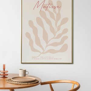 May include: A beige and pink abstract art print with the text "Matisse" and "THE CUT-OUTS Du Vendredi 27 Fevrier au Samedi 28 Mars 1952" in a gold frame.
