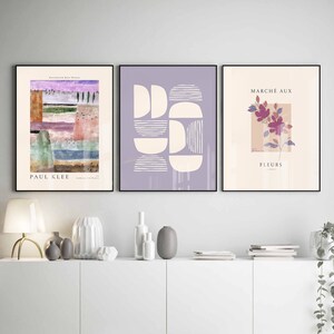 May include: Three framed art prints with abstract designs. The left print features a colourful abstract landscape with the text "PAUL KLEE" at the bottom. The middle print features a geometric design with white shapes on a light purple background. The right print features a pink flower with the text "MARCH&Eacute; AUX FLEURS" at the top.