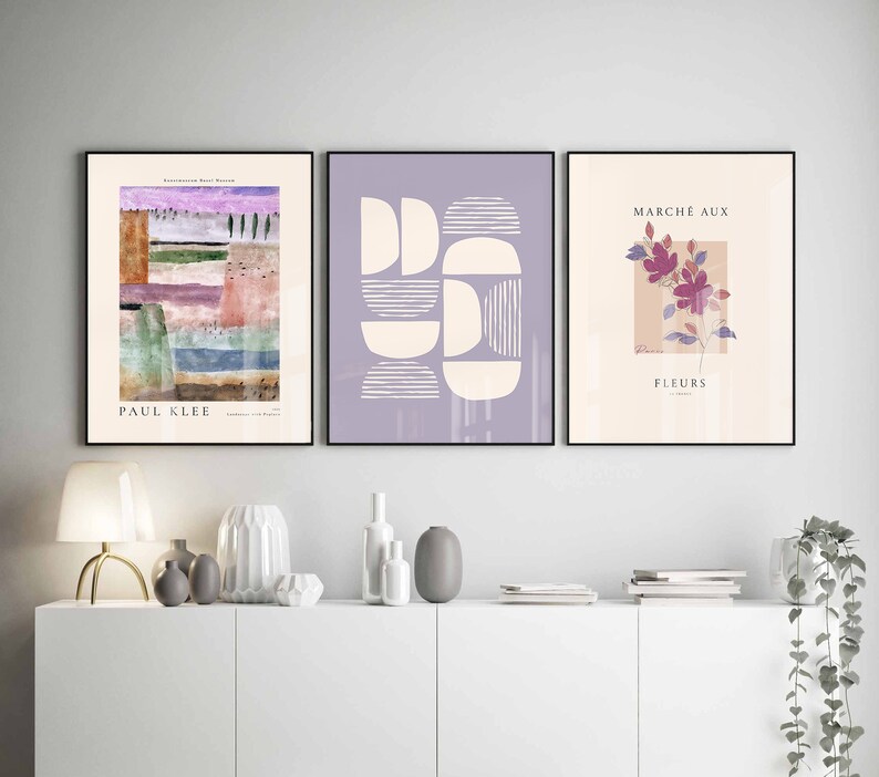 May include: Three framed art prints with abstract designs. The left print features a colourful abstract landscape with the text "PAUL KLEE" at the bottom. The middle print features a geometric design with white shapes on a light purple background. The right print features a pink flower with the text "MARCH&Eacute; AUX FLEURS" at the top.