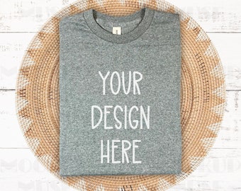 May include: A heather gray t-shirt with the text "YOUR DESIGN HERE" on a woven wicker placemat.